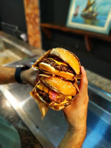person-holding-two-burgers-3630141.jpg